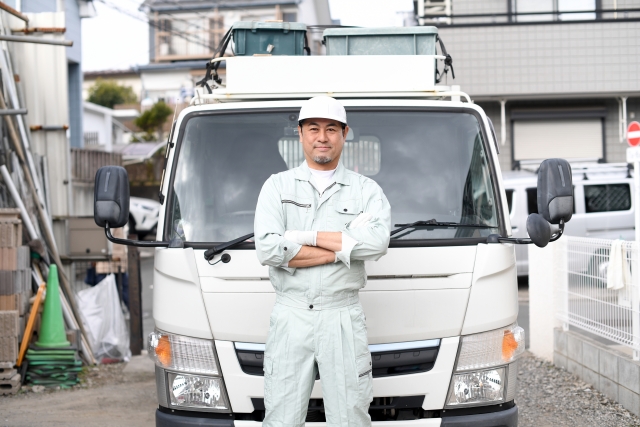 トラックの前で腕組みをして立ってる作業員